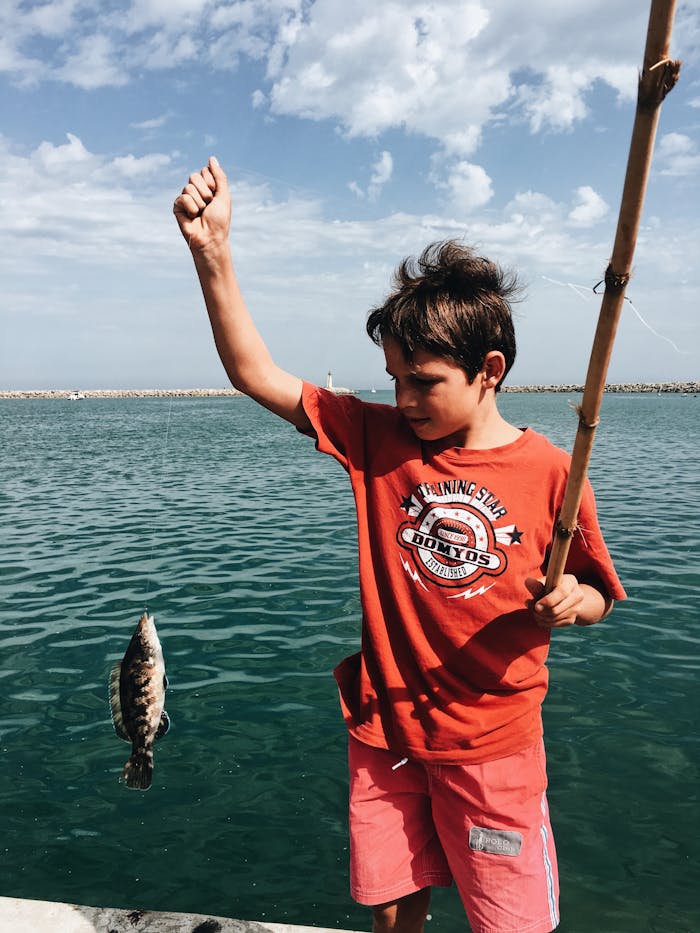 Young boy celebrates catching a fish on a sunny day by the sea.