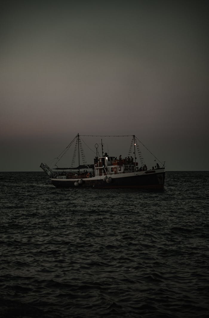 A fishing boat sails on the open sea at twilight, with dim lighting capturing a serene maritime scene.