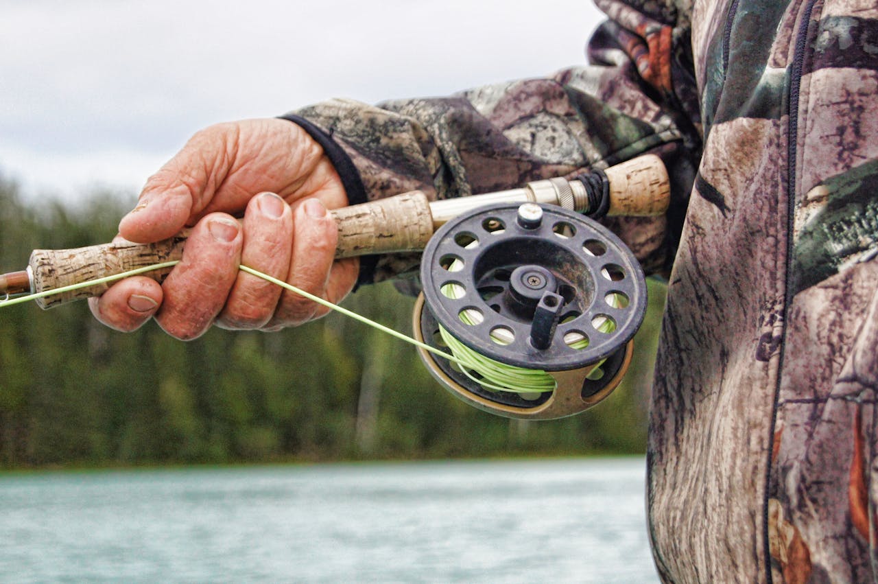 Detailed view of a fisherman handling a fishing rod by a river in Alaska.