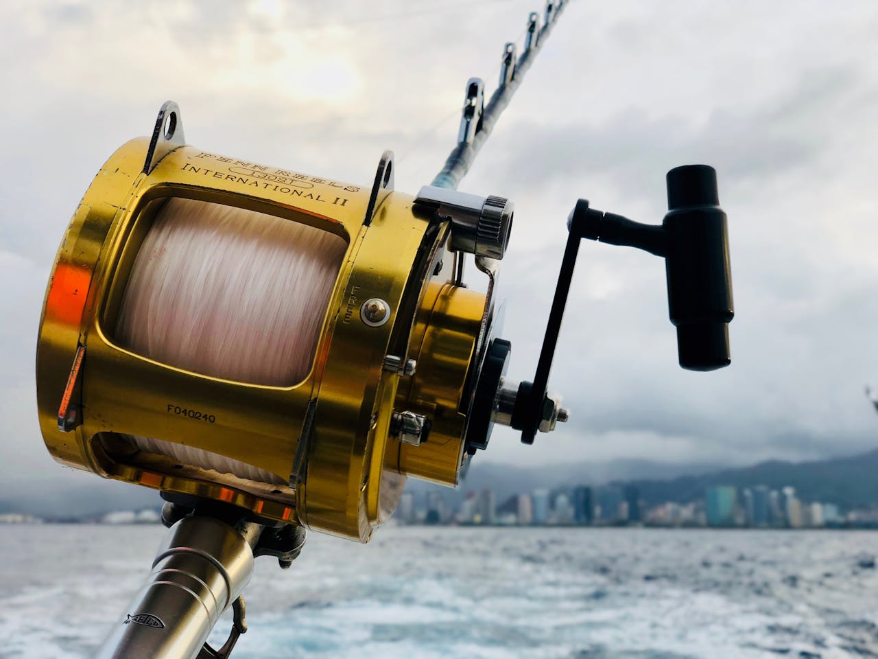 Close-up of a fishing rod and reel over the ocean with the Honolulu skyline in the background.